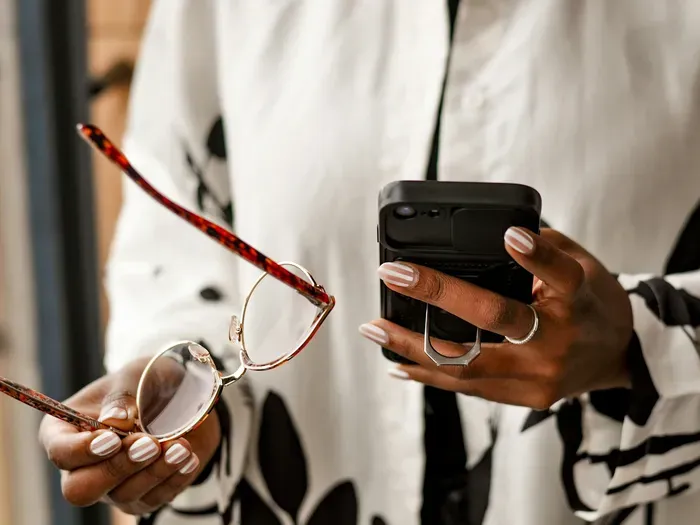 Hands holding eyeglasses and a smartphone with wallet case, exploring local services on Local Biz Guide Now